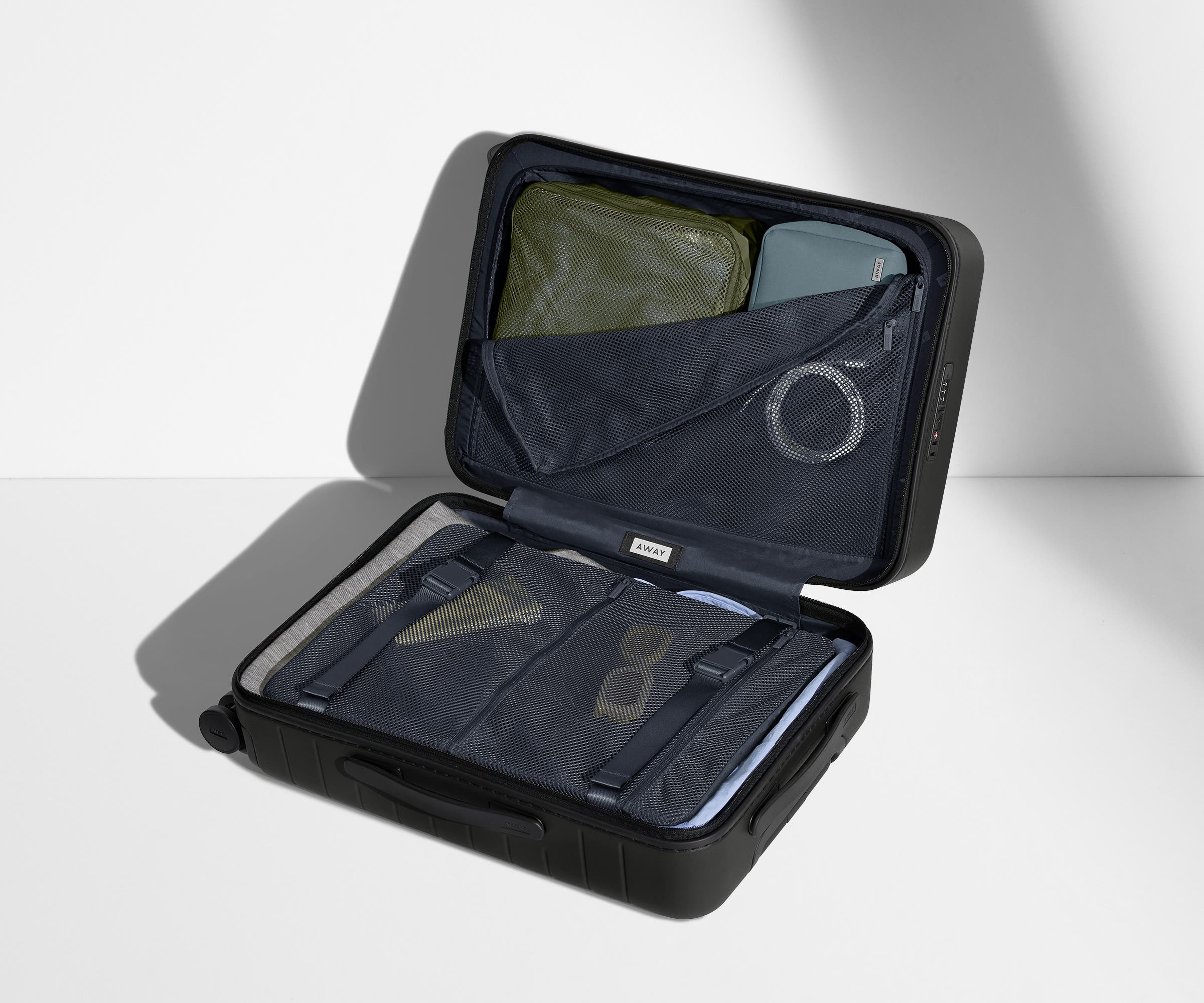 The Bigger Carry-On suitcase in Jet Black shown open on its side and packed with Away's packing organizers to show capacity and the interior compression system, designed to help you pack more in