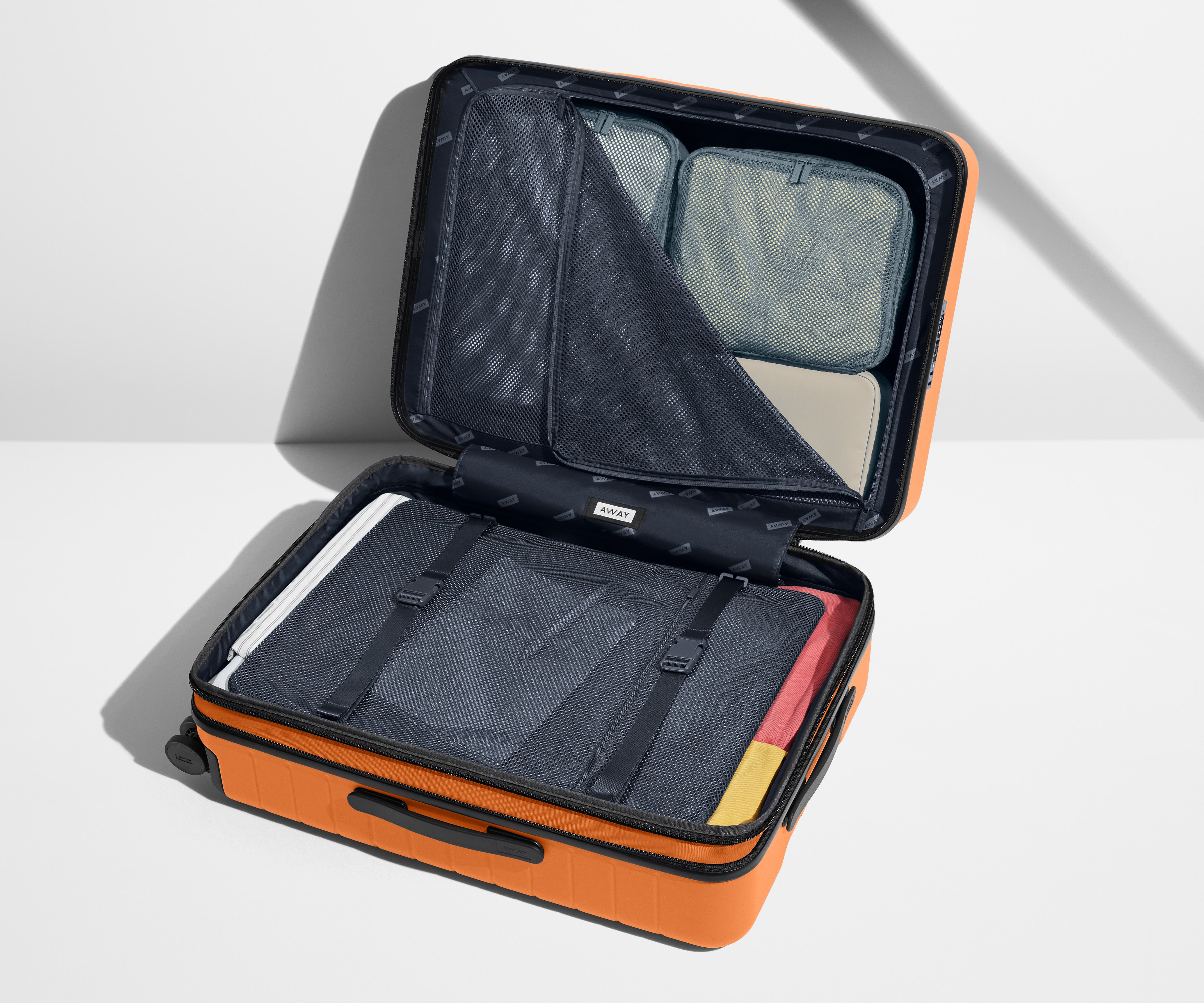 The Medium Flex suitcase in Sorbet Orange shown open on its side and packed with Away's packing organizers to show capacity and the interior compression system, designed to help you pack more in