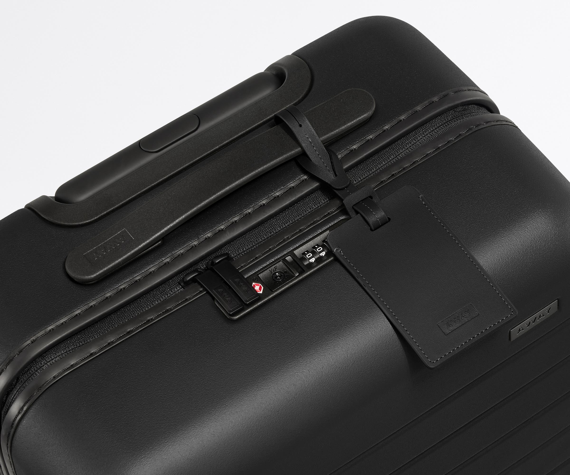 The Bigger Carry-On suitcase in Jet Black shown shown from above highlighting TSA-approved combination lock and recycled leather luggage tag