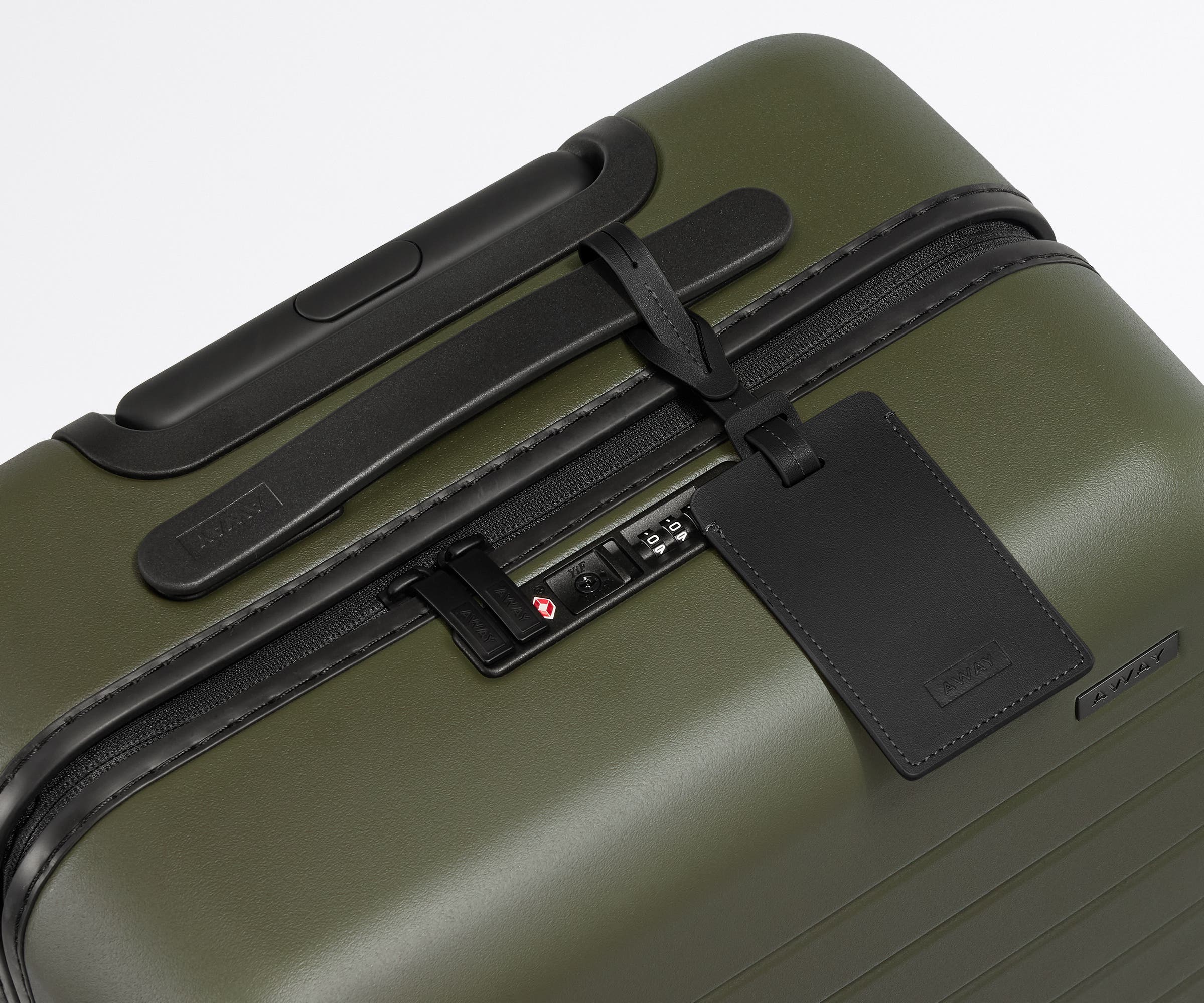 The Bigger Carry-On suitcase in Olive Green shown shown from above highlighting TSA-approved combination lock and recycled leather luggage tag