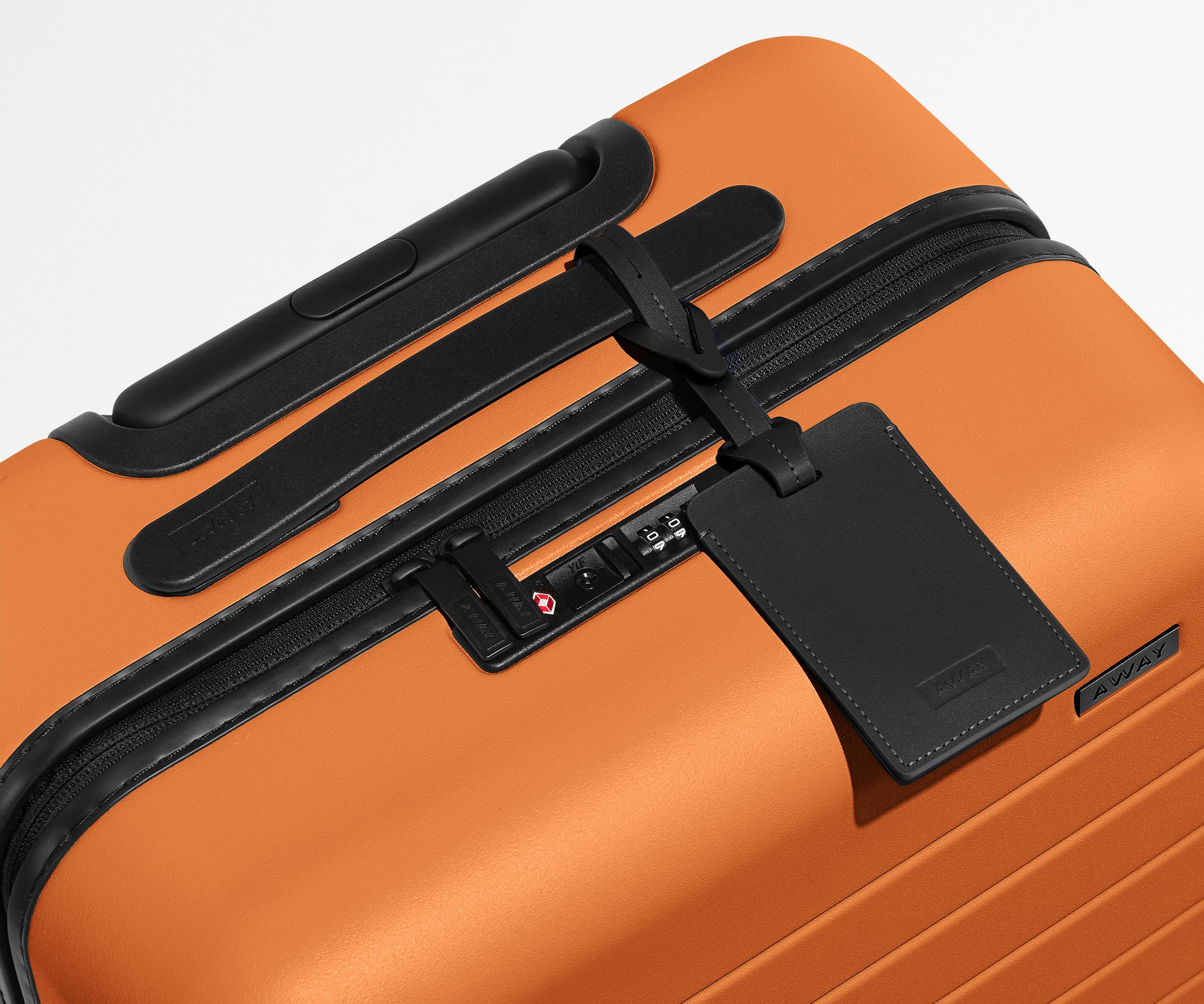 The Bigger Carry-On suitcase in Sorbet Orange shown shown from above highlighting TSA-approved combination lock and recycled leather luggage tag