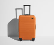 Front product view of The Bigger Carry-On suitcase in Sorbet Orange with raised handle