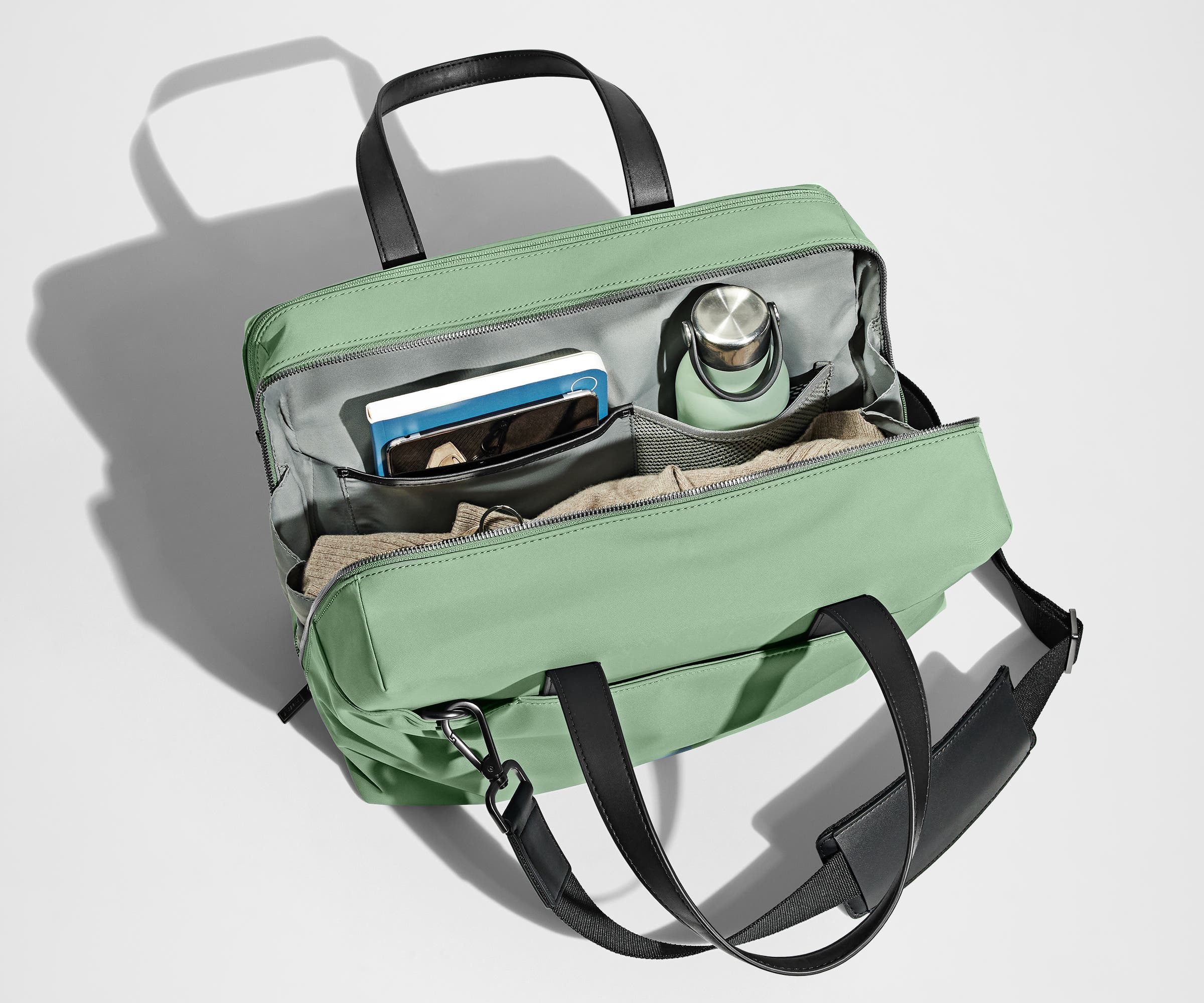 Main compartment packed with a light sweater, notebook, tablet, and water bottle. The detachable shoulder strap is clipped onto the bag.