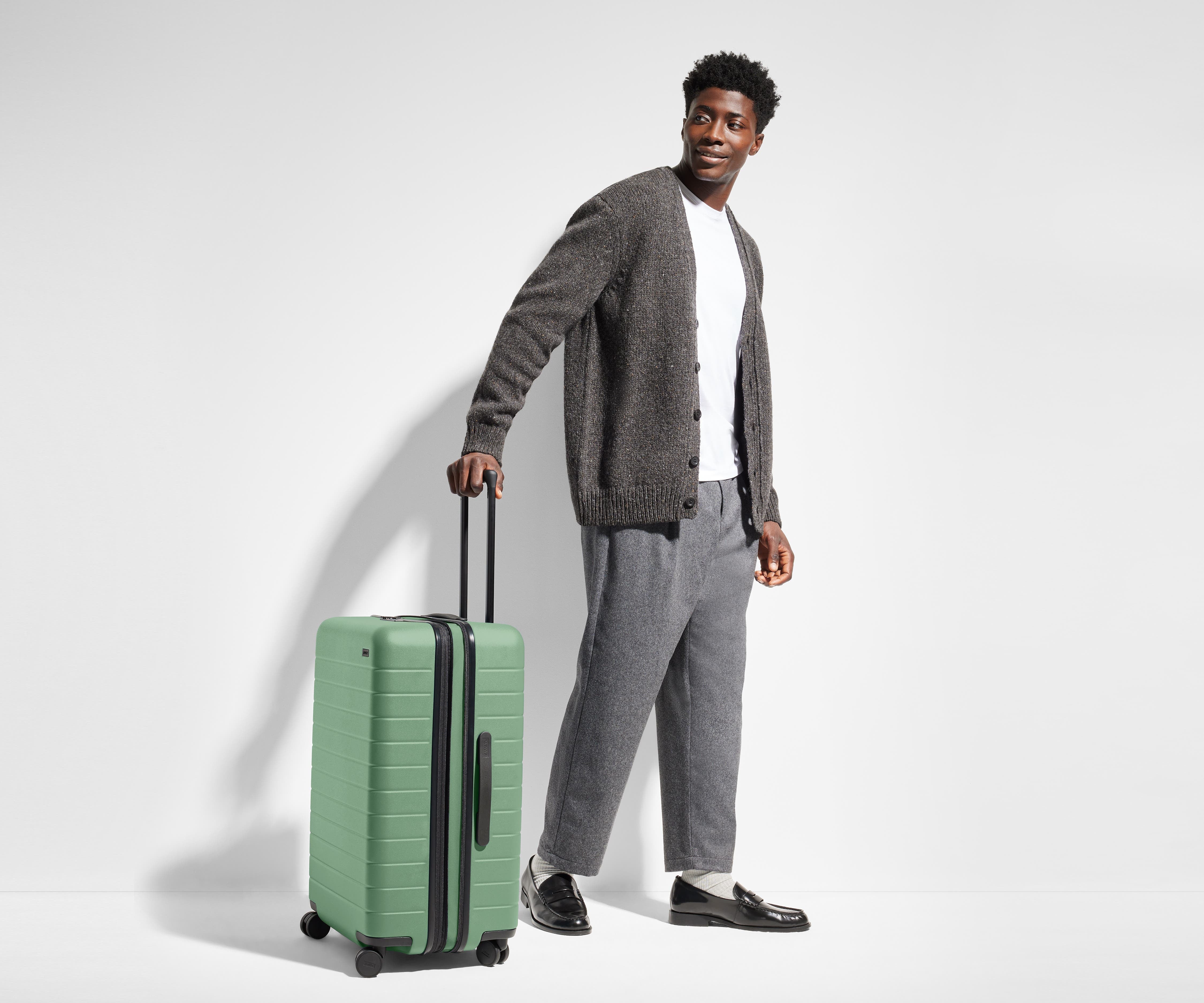 Male-presenting person standing next to a Medium Flex suitcase for scale