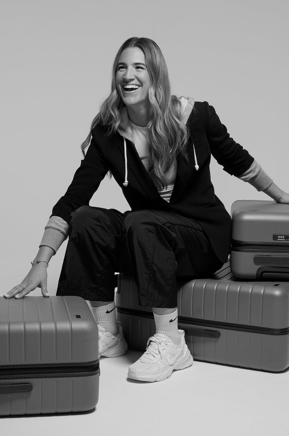 A black and white photo of Sabrina sitting on some Away suitcases