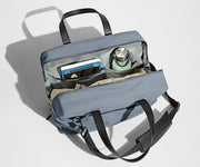Main compartment packed with a light sweater, notebook, tablet, and water bottle. The detachable shoulder strap is clipped onto the bag.
