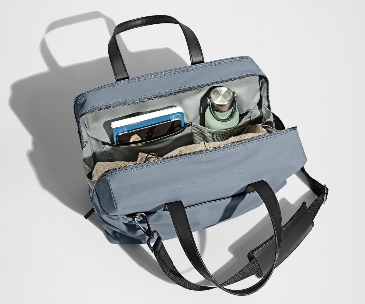 Main compartment packed with a light sweater, notebook, tablet, and water bottle. The detachable shoulder strap is clipped onto the bag.