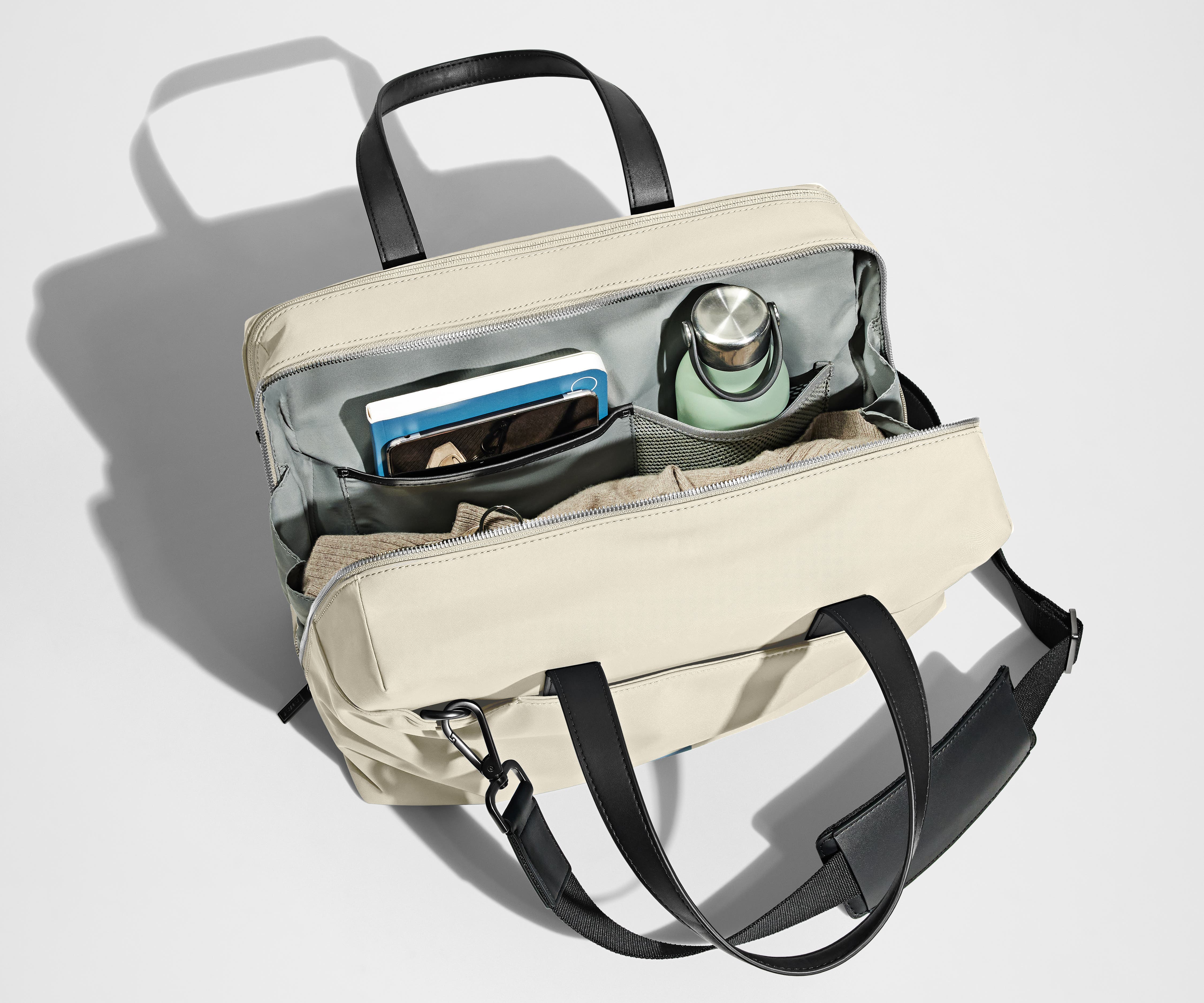 Main compartment packed with a light sweater, notebook, tablet, and water bottle. The detachable shoulder strap is clipped onto the bag.