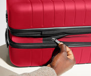 Red suitcase with a hand zipping it closed on a light background