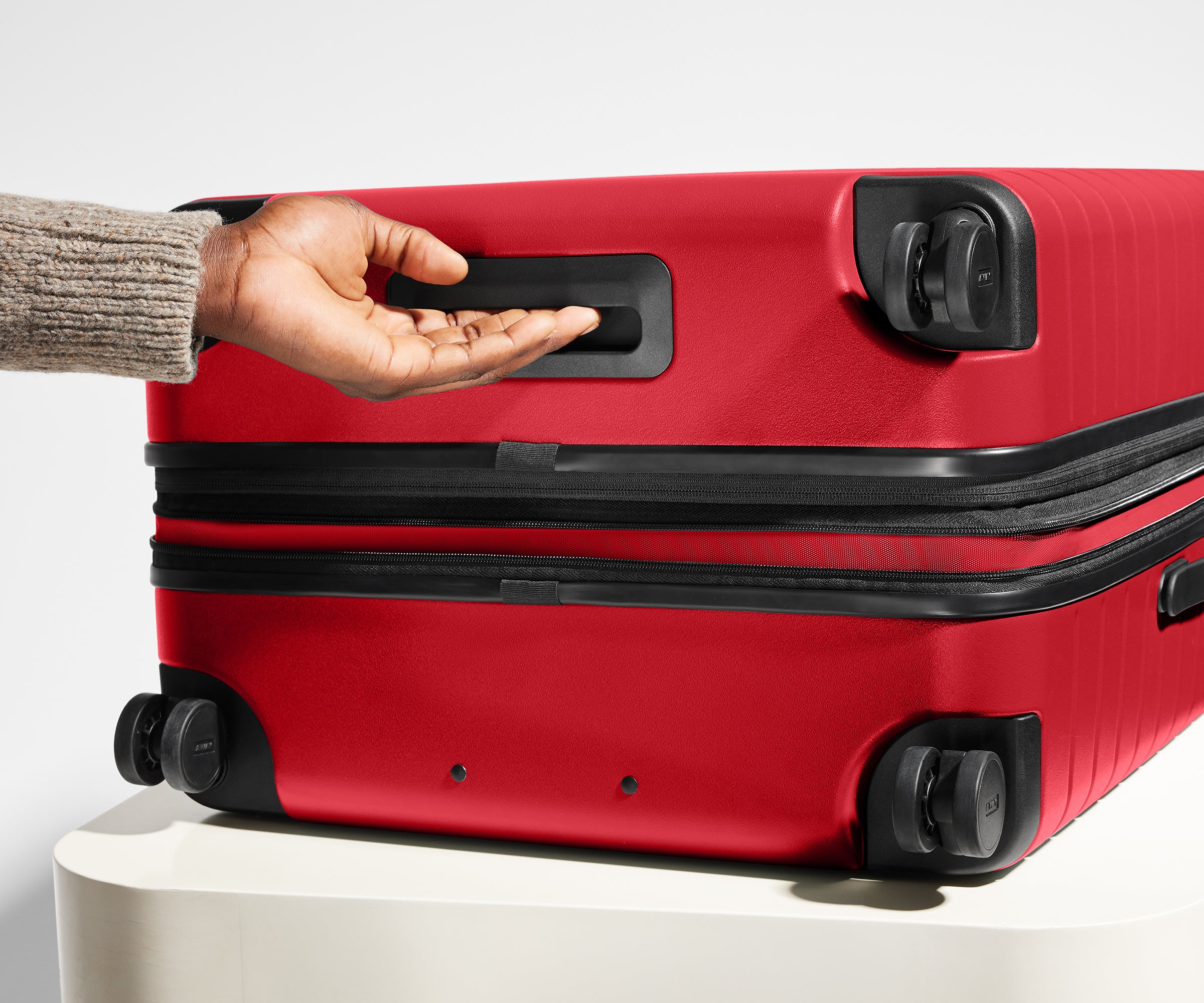 Red suitcase with a hand on its handle against a neutral background