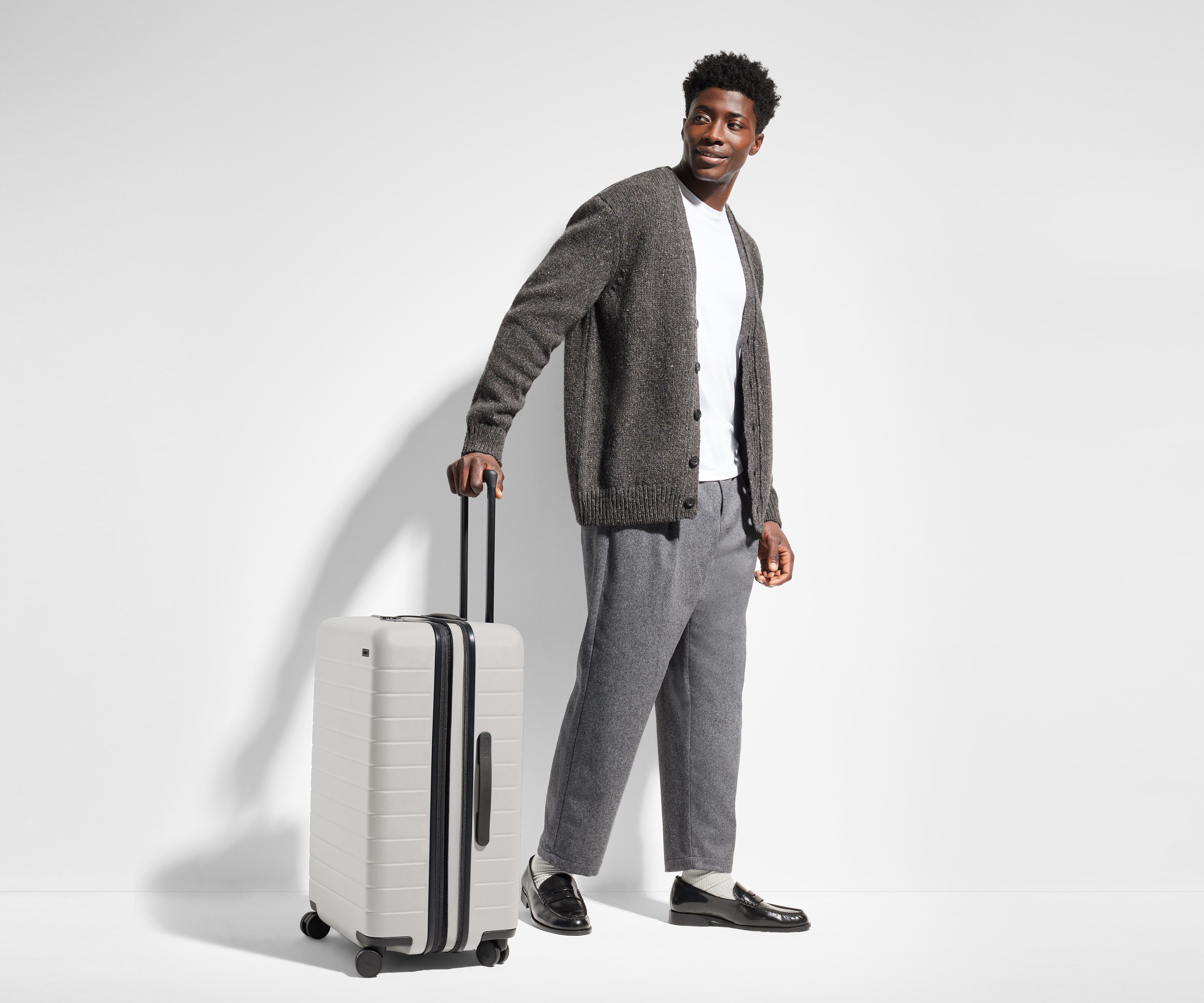 Male-presenting person standing next to a Medium Flex suitcase for scale