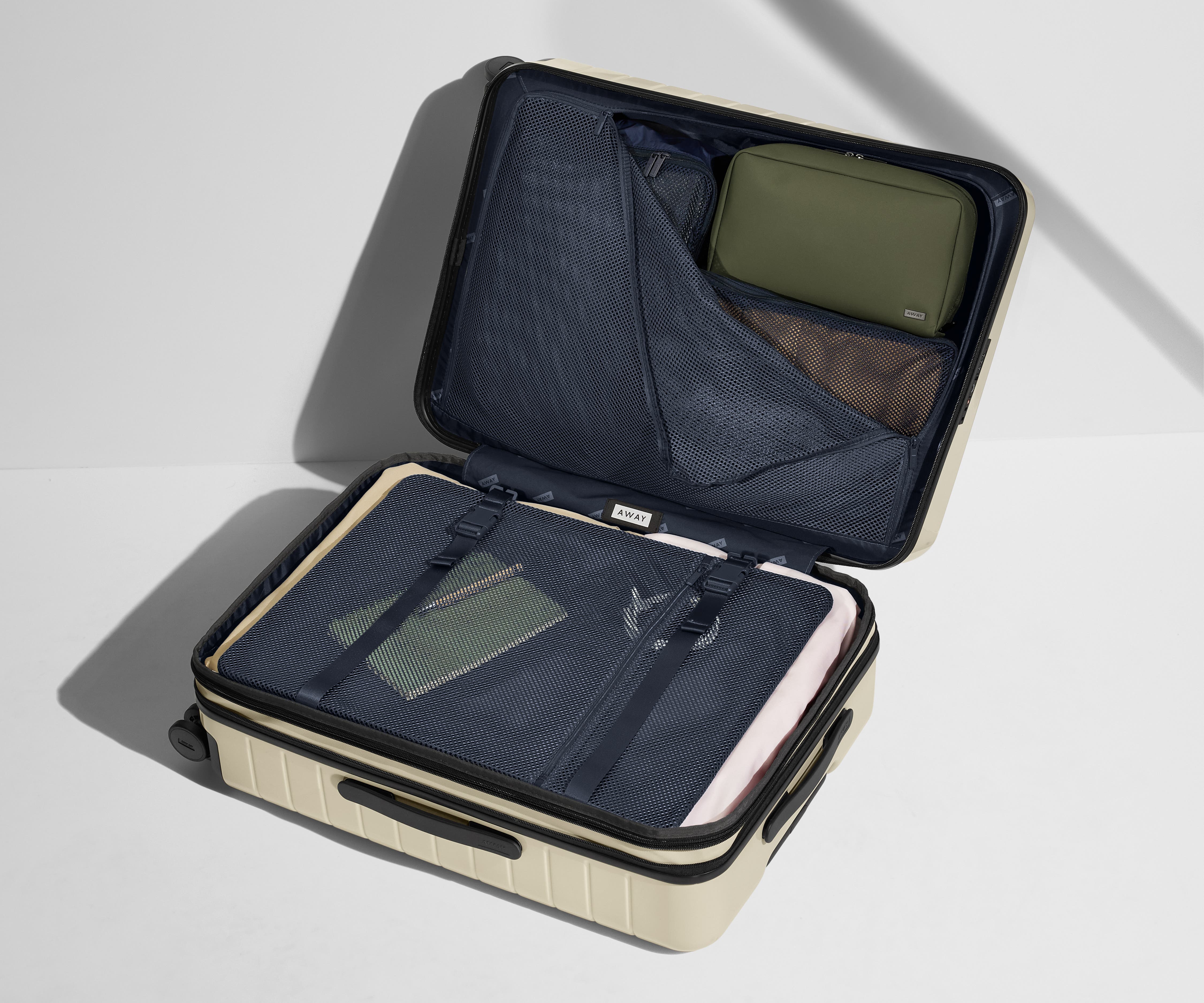 The Medium Flex suitcase in Salt White shown open on its side and packed with Away's packing organizers to show capacity and the interior compression system, designed to help you pack more in