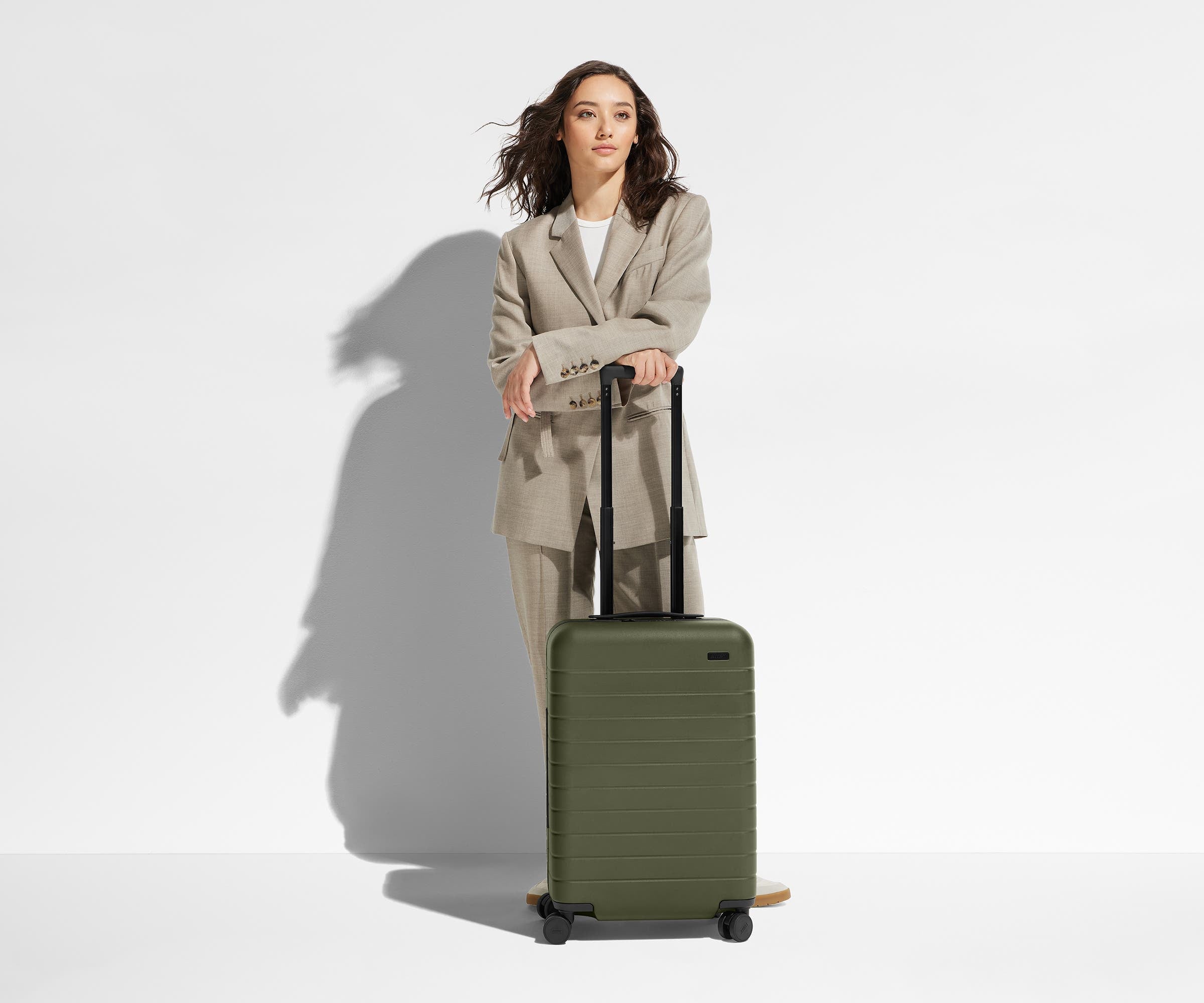 A 5'6" female model is standing next to The Bigger Carry-On suitcase and leaning her arms on the raised handle to show size and scale
// 
Model is 5'6"
