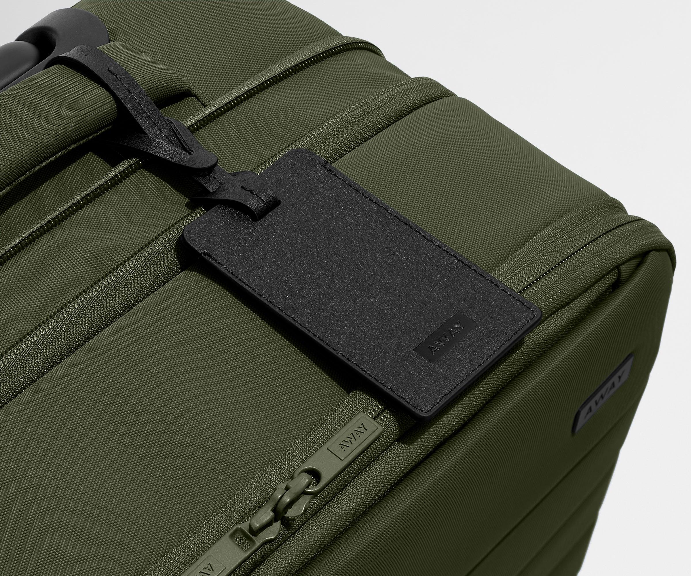 The Softside Carry-On suitcase in Olive Green shown shown from above highlighting the recycled leather luggage tag and expansion feature