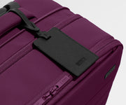 The Softside Bigger Carry-On suitcase in Plum Purple shown shown from above highlighting the recycled leather luggage tag and expansion feature